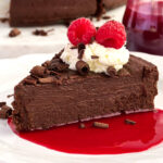 A slice of a flourless chocolate torte topped with whipped cream and raspberries.