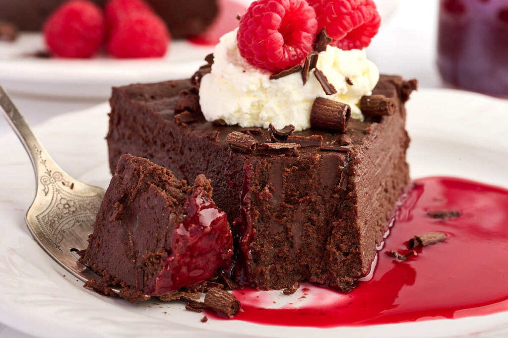 Chocolate cake slice with cream, raspberries, raspberry sauce, and a forkful.