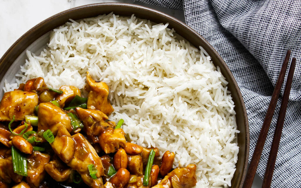 Bowl of rice with stir-fried chicken, peanuts, green onions, and chopsticks.