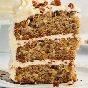 Three-layer cake slice with white frosting and nuts on a plate with fork.