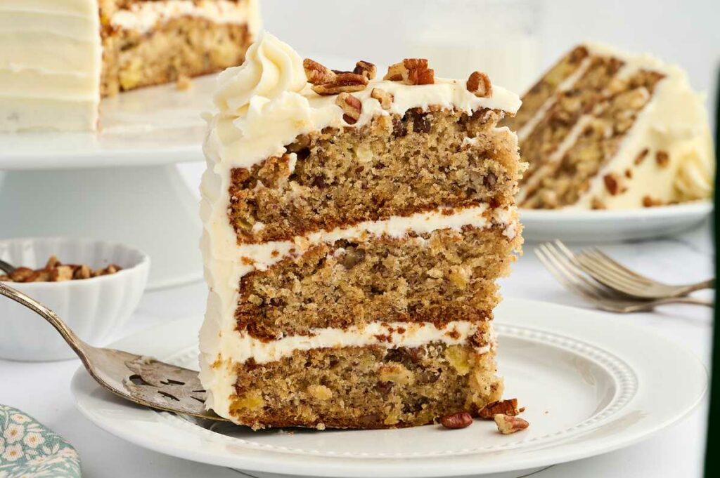 Two slices of hummingbird cake on plates next to the layer cake.