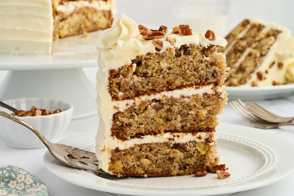 Two slices of hummingbird cake on plates next to the layer cake.