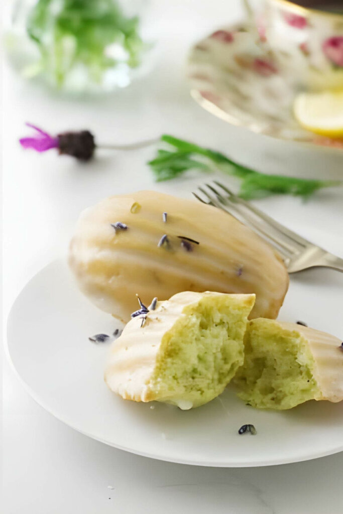 Two madeleine cookies on a plate topped with lavender buds.