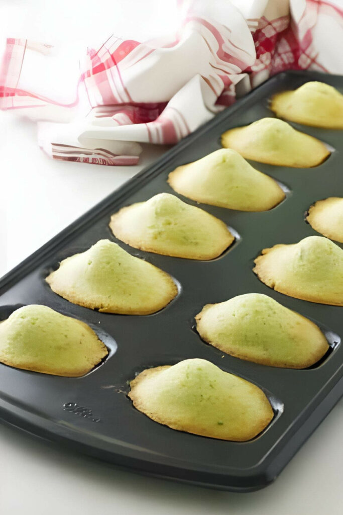Tray of lavender madeleines with humps on white surface by red-white towel.