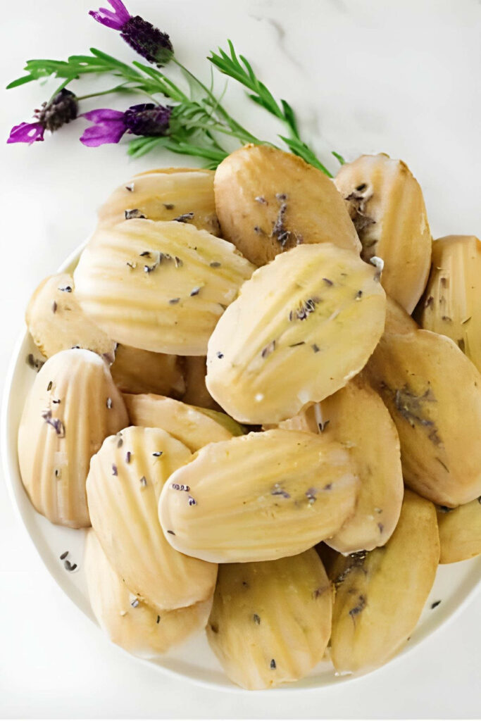 Madeleine cookies with icing and dried lavender, fresh lavender sprigs beside plate.