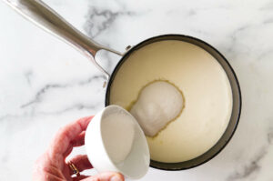 Pouring sugar into a pot of cream.