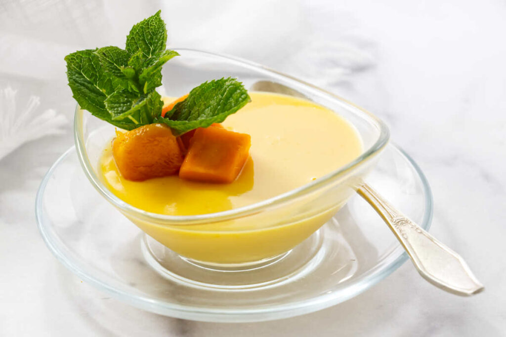 A posset dessert in a dish topped with slices of mango and mint.