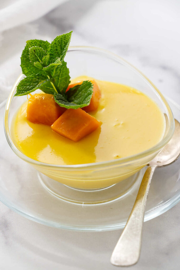 A mango posset cream dessert in a clear dish topped with mango.