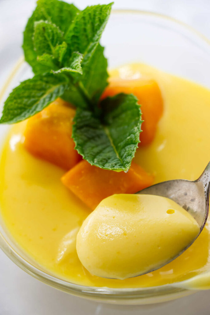Glass bowl of mango cream dessert topped with mango cubes and mint.