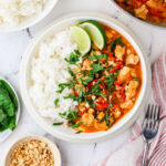 A dish with white rice and peanut butter chicken curry topped with basil.