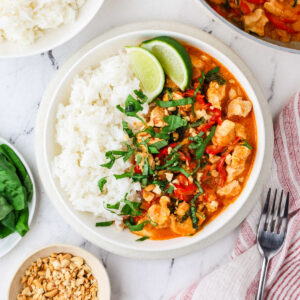 A dish with white rice and peanut butter chicken curry topped with basil.