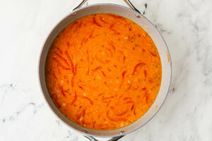 Skillet with creamy curry sauce and sliced red bell peppers.