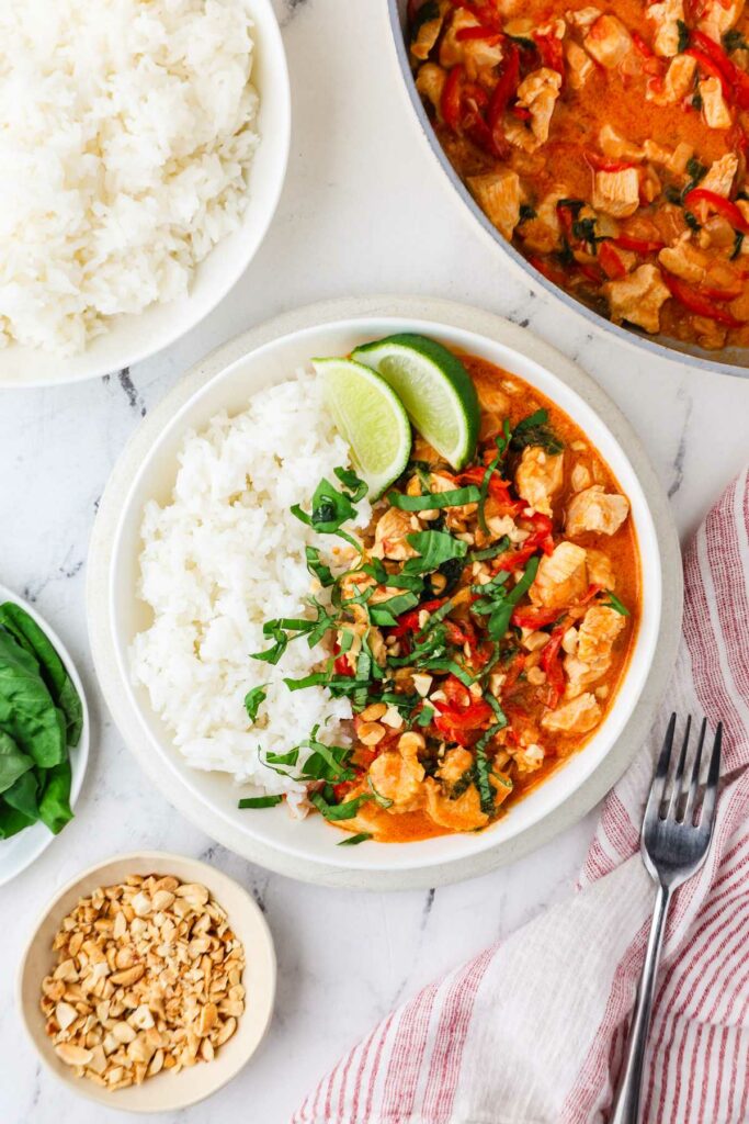 Plate of white rice and peanut curry with chicken, lime, and herbs.