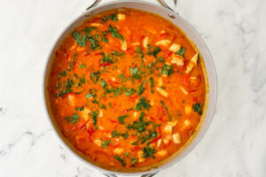 A peanut curry sauce with chicken in a skillet.