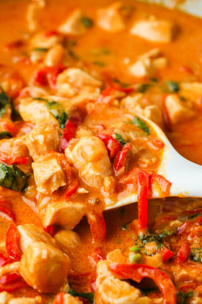 A spoon scooping up chicken curry and sauce made with peanut butter.