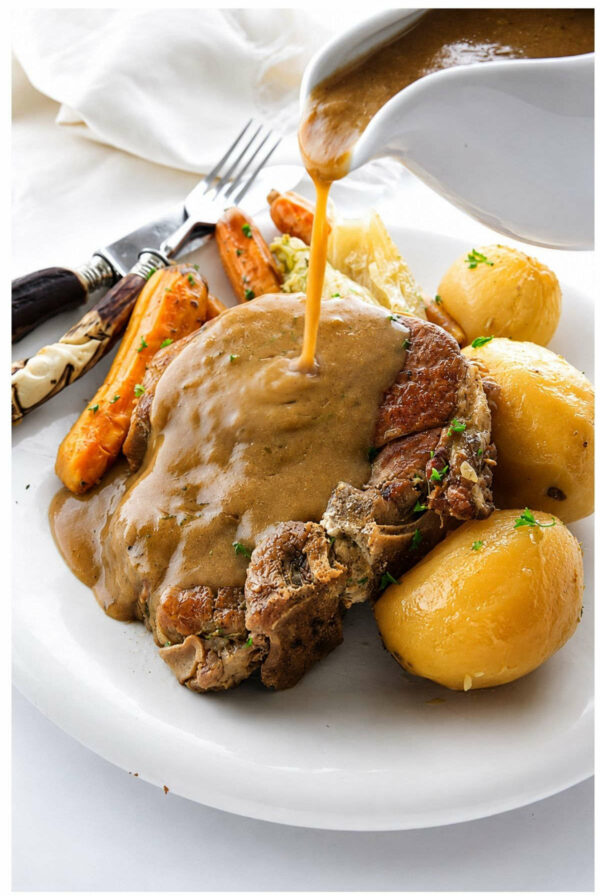 Pouring gravy over pork chops on a plate with potatoes.