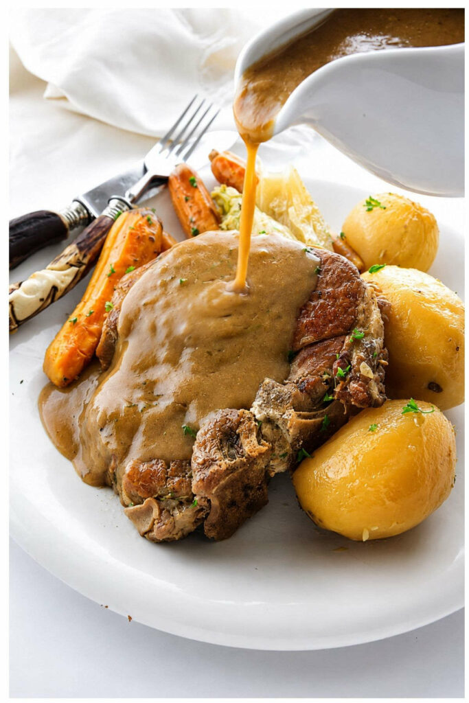Pouring gravy over pork chops on a plate with potatoes.