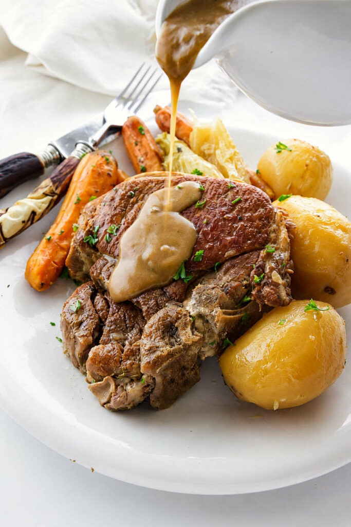 Gravy being poured over pork chop with potatoes and carrots on a plate.