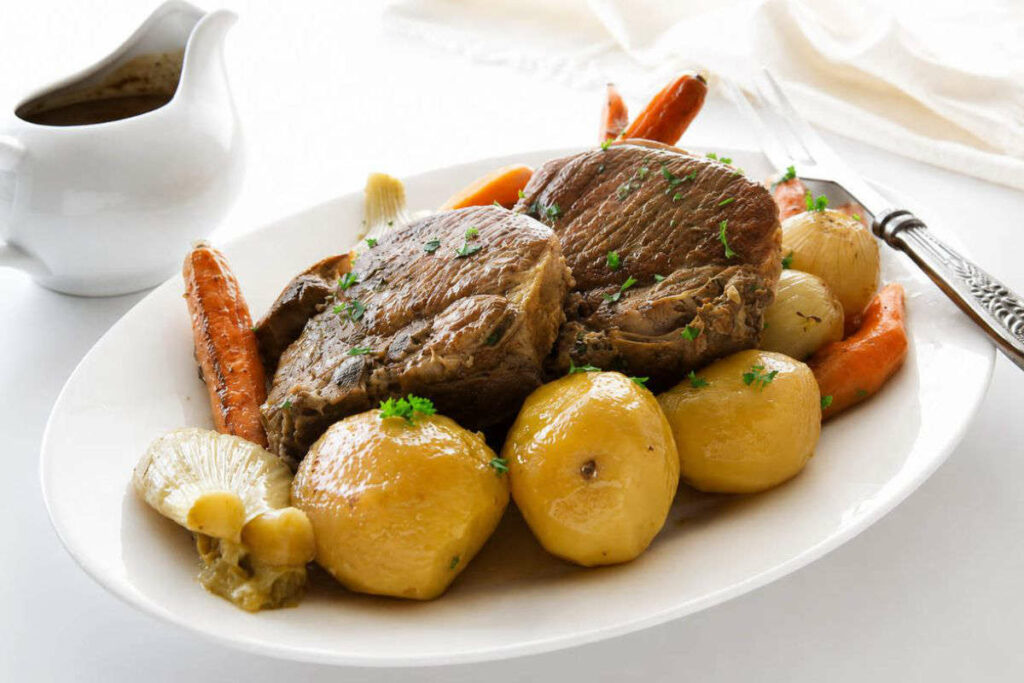 A serving platter with pork chops and vegetables in front of a pitcher of gravy.