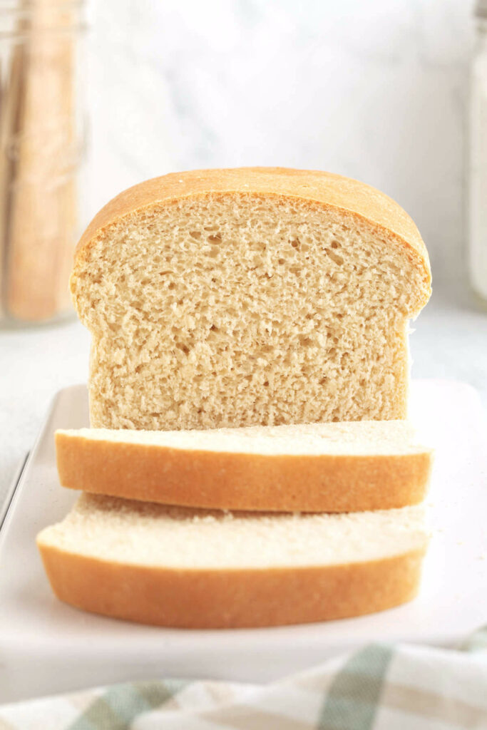 A loaf of white sandwich bread on a white counter with slices in front.