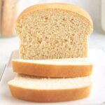 Homemade sandwich bread with golden crust and two slices on white surface.