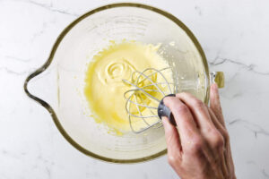 Whipping egg yolks and sugar in a glass mixing bowl.
