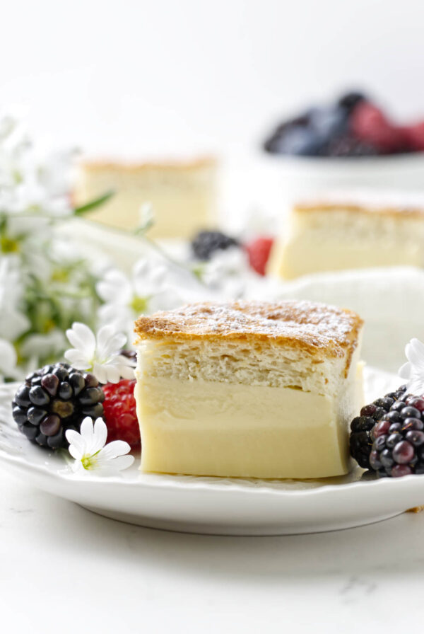 A slice of a 3 layer vanilla custard cake on a plate next to fresh berries.