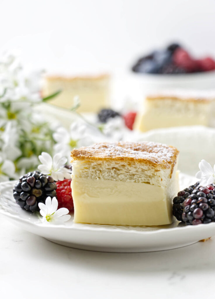 A slice of a 3 layer vanilla custard cake on a plate next to fresh berries.
