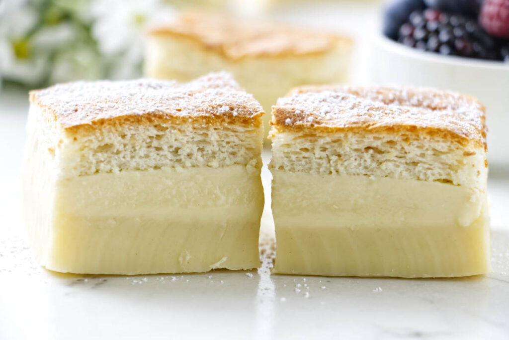 Two custard cakes with golden tops on white surface; berries blurred behind.