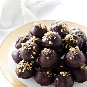 Chocolate truffles with nuts on a gold-rimmed plate, white background.