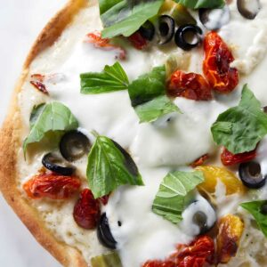 Close-up of a pizza with mozzarella, olives, sun-dried and yellow tomatoes, basil.