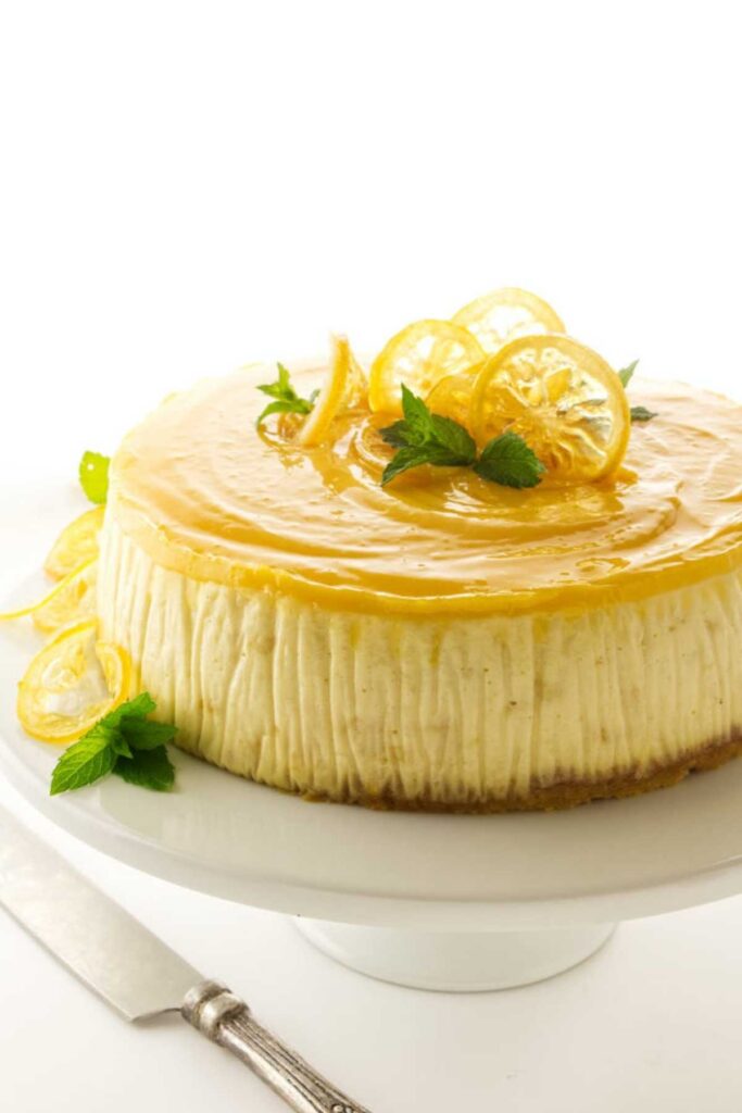 Lemon cheesecake with lemon slices and mint on a white cake stand.