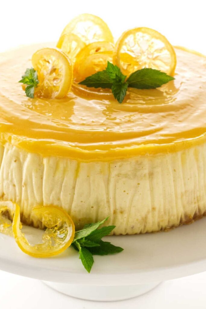 Lemon cheesecake with lemon curd, candied lemon, and mint on a white stand.