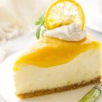 Lemon cheesecake slice with toppings on white plate and green-handled fork.
