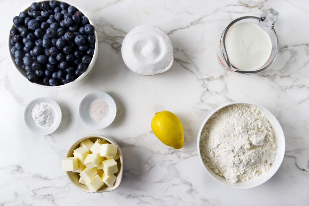 Ingredients for blueberry cobbler with fresh blueberries, lemon, butter, flour, and cream.