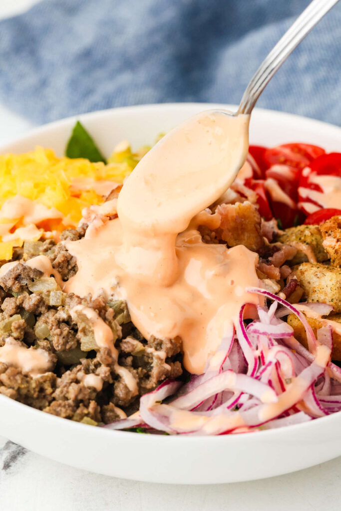 Close-up of cheeseburger salad with melted cheddar, tomatoes, and sliced pickles.