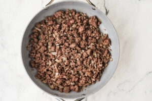 Overhead view of a cheeseburger salad bowl with ground beef, onion, and cheese.