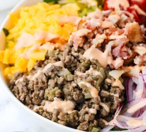 Homemade cheeseburger salad served in a white bowl with Thousand Island dressing on the side.
