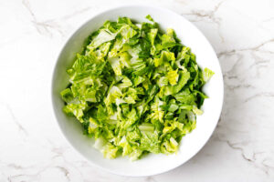 White bowl of fresh chopped romaine lettuce on a white marble surface.