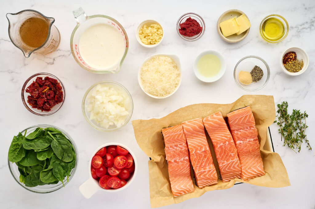 Top-down view of salmon, spinach, tomatoes, and various cooking ingredients on white surface.