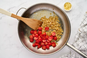 Metal skillet with sautéed onions, tomatoes, and spatula.