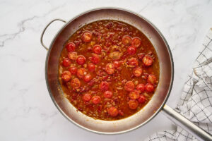 Stirring broth into the tomato mixture to make a sauce.