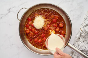 Adding cream and parmesan cheese to the sauce in a skillet.