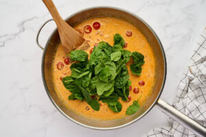 Adding fresh spinach to the tomato cream sauce.
