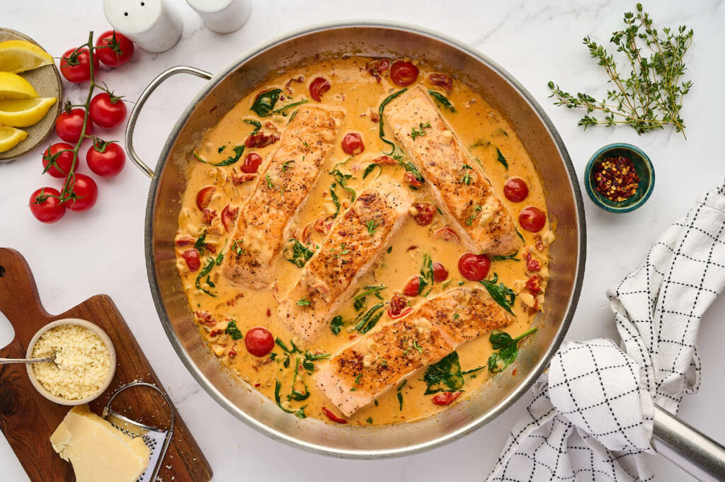 Skillet of creamy Tuscan salmon with cherry tomatoes and spinach in cream sauce.