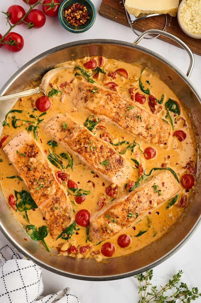 Salmon fillets in creamy sauce with tomatoes and spinach in a skillet.