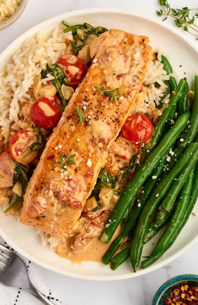 Grilled salmon in creamy tomato sauce over rice with beans and spinach.