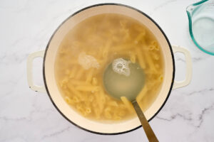 A ladle reserving hot pasta water before draining the water.