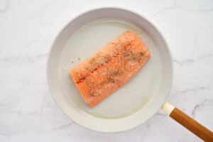 Searing a salmon fillet in a skillet.