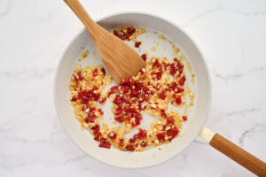 Cooking shallots and sun dried tomatoes in a skillet.
